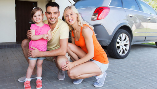 Family posing by their car in the driveway.